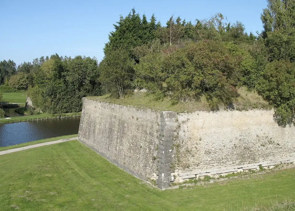 Un mur des remparts au bord de l’eau, entouré de pelouses et d’arbres.